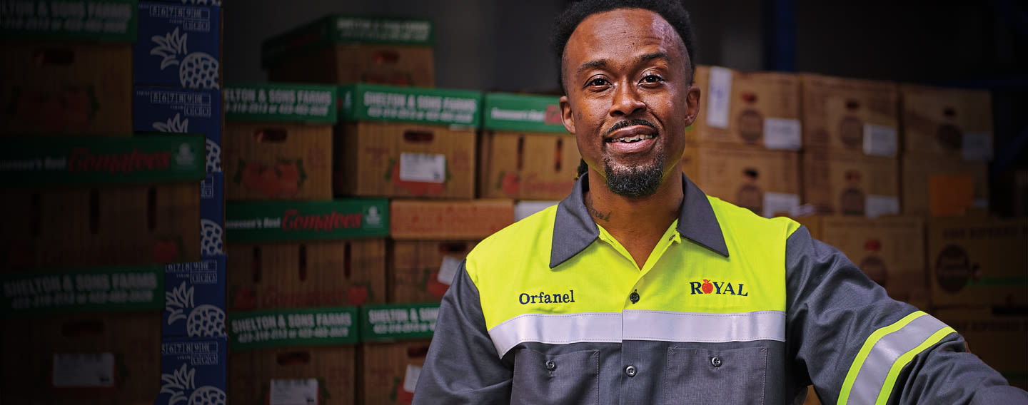 Man in safety uniform smiling in a warehouse with stacked boxes.