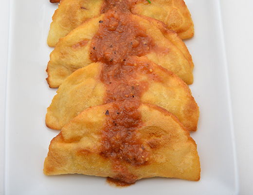 Five golden empanadas topped with a red sauce on a white plate.