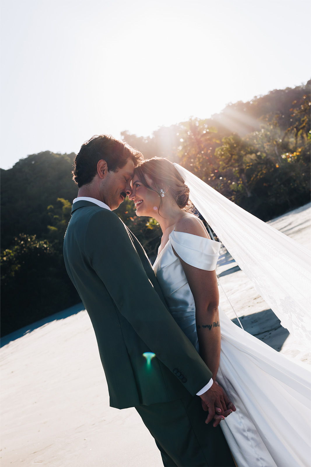 Couple in wedding attire sharing a tender moment outdoors at sunset.