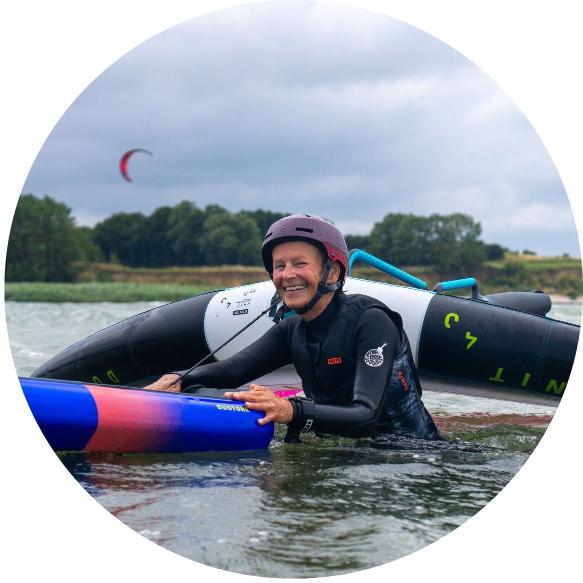 Person in a wetsuit smiling while holding a board in water.