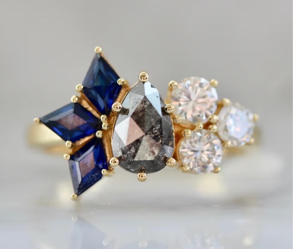 Asymmetrical engagement ring with pear shaped salt and pepper diamond, kite cut blue sapphires, and round brilliant diamonds