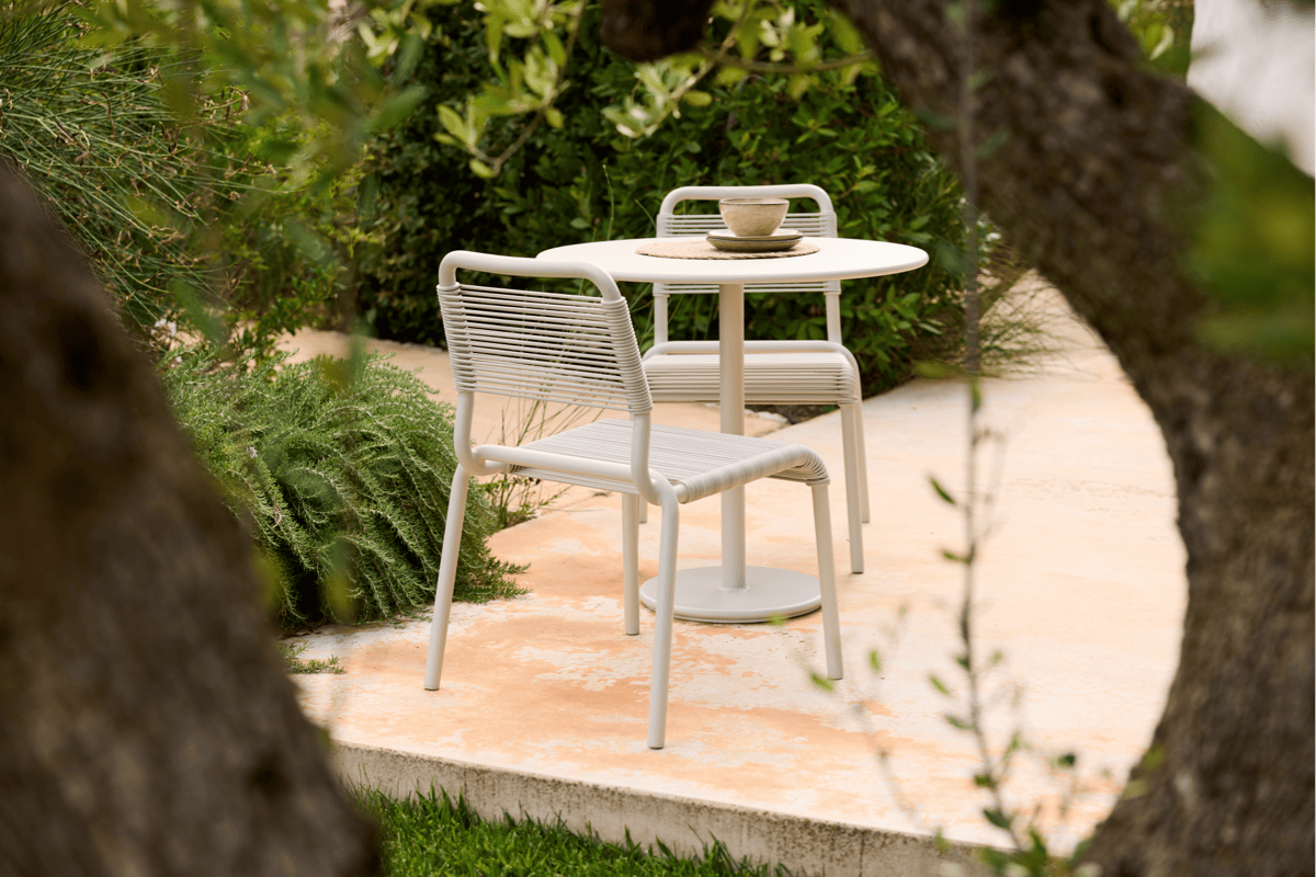 Small white outdoor bistro set with round dining table and two chairs in a garden patio setting.