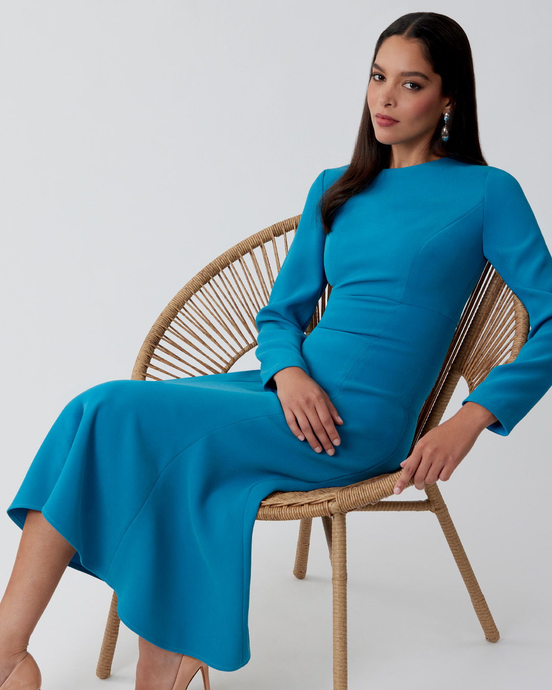 Woman in a blue dress sitting on a rattan chair.