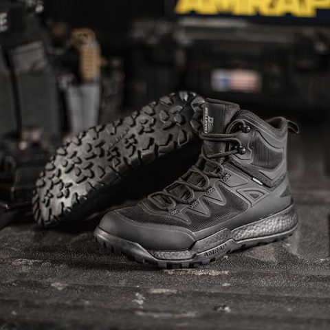 Black tactical boots displayed on a dark surface with equipment in background.