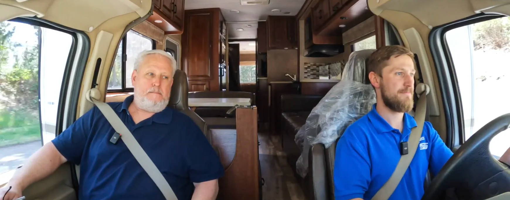 Two men sitting in an RV, one driving and one passenger.