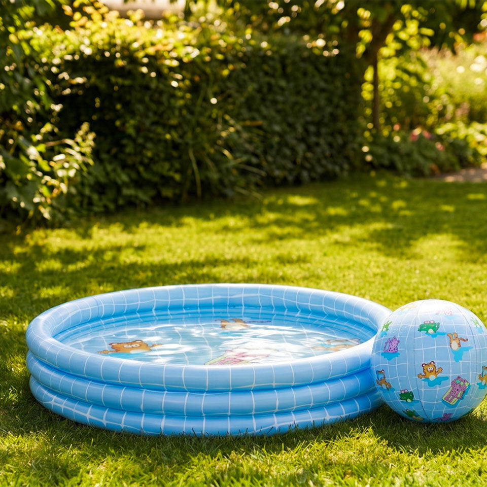 Inflatable pool and beach ball on green grass in a sunny garden.