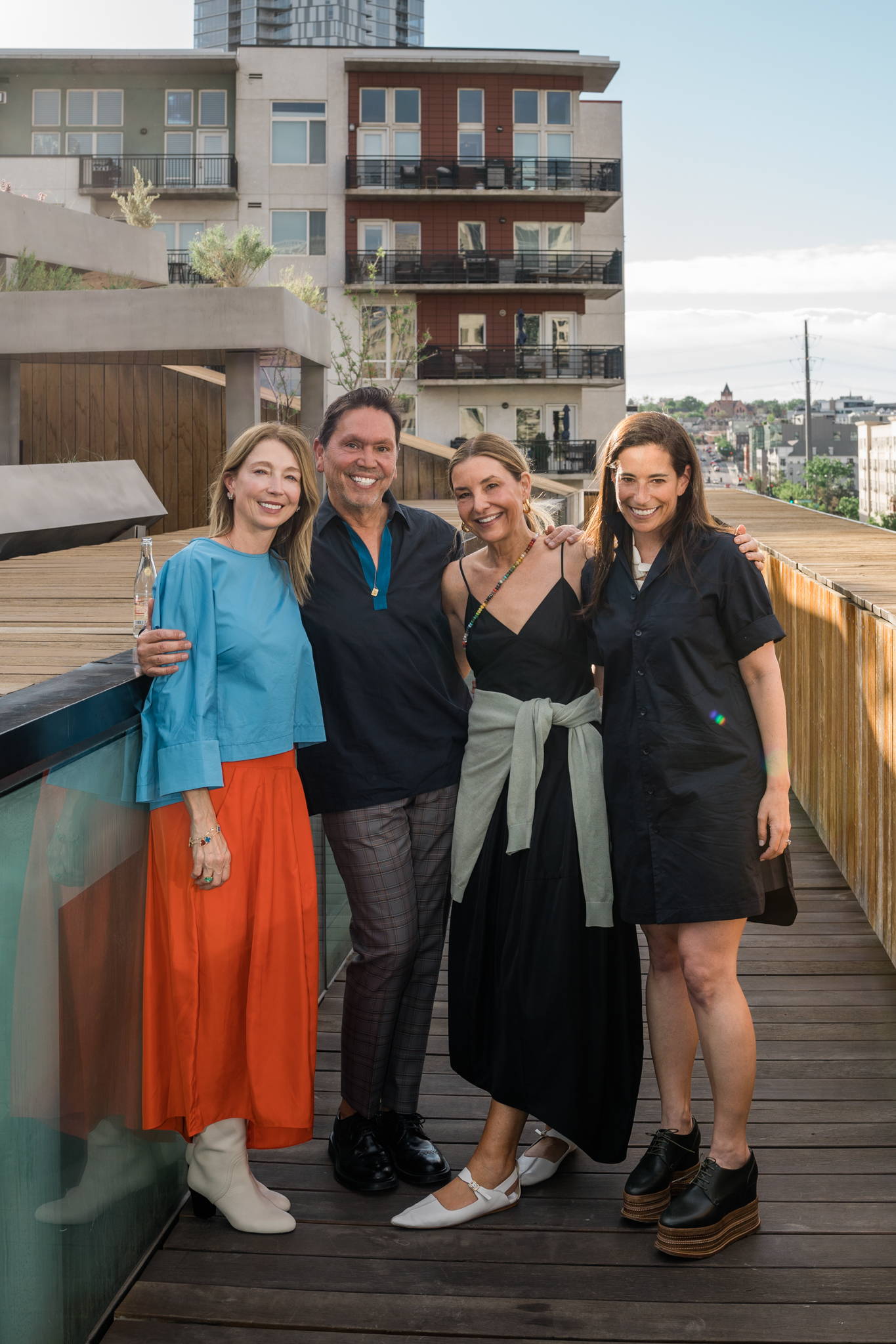 Four people posing together on a balcony with modern buildings in the background.