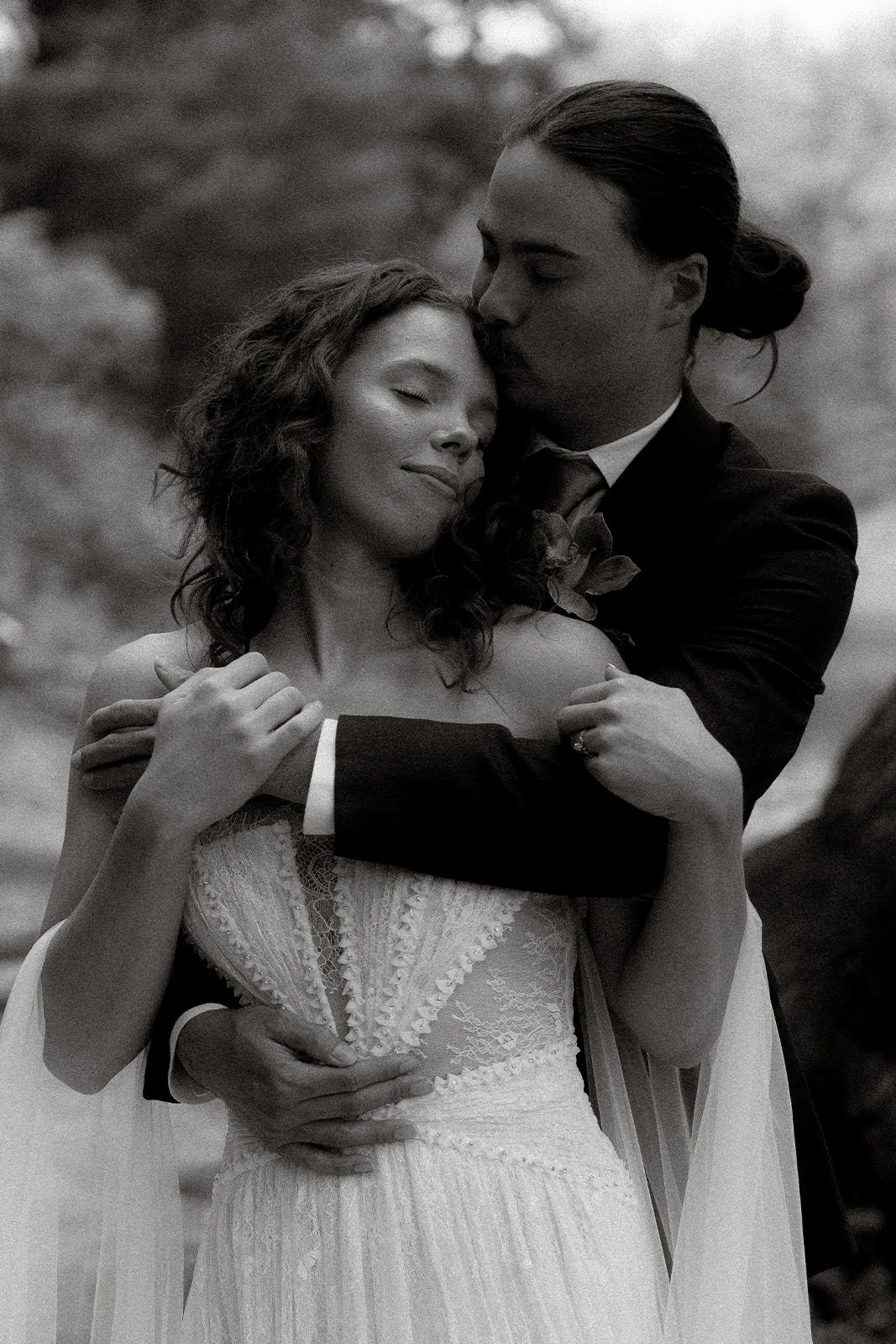 A couple embracing, dressed in wedding attire, in a romantic outdoor setting.
