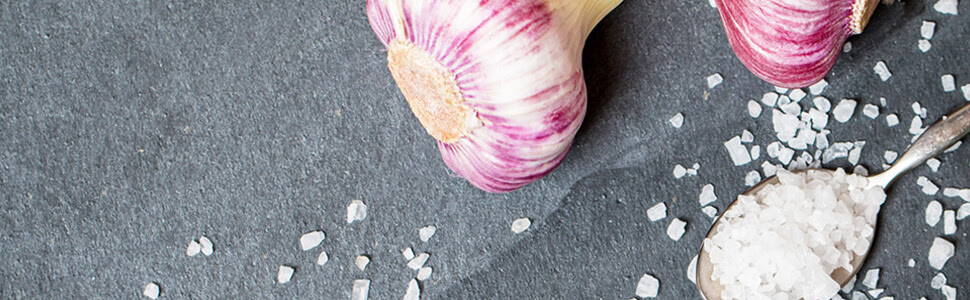 pink garlic bulb on a stone table with spoonful of kosher salt