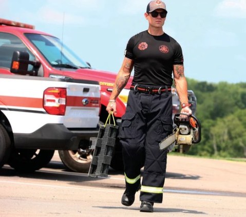 Firefighter walking with equipment near a fire truck on a sunny day.