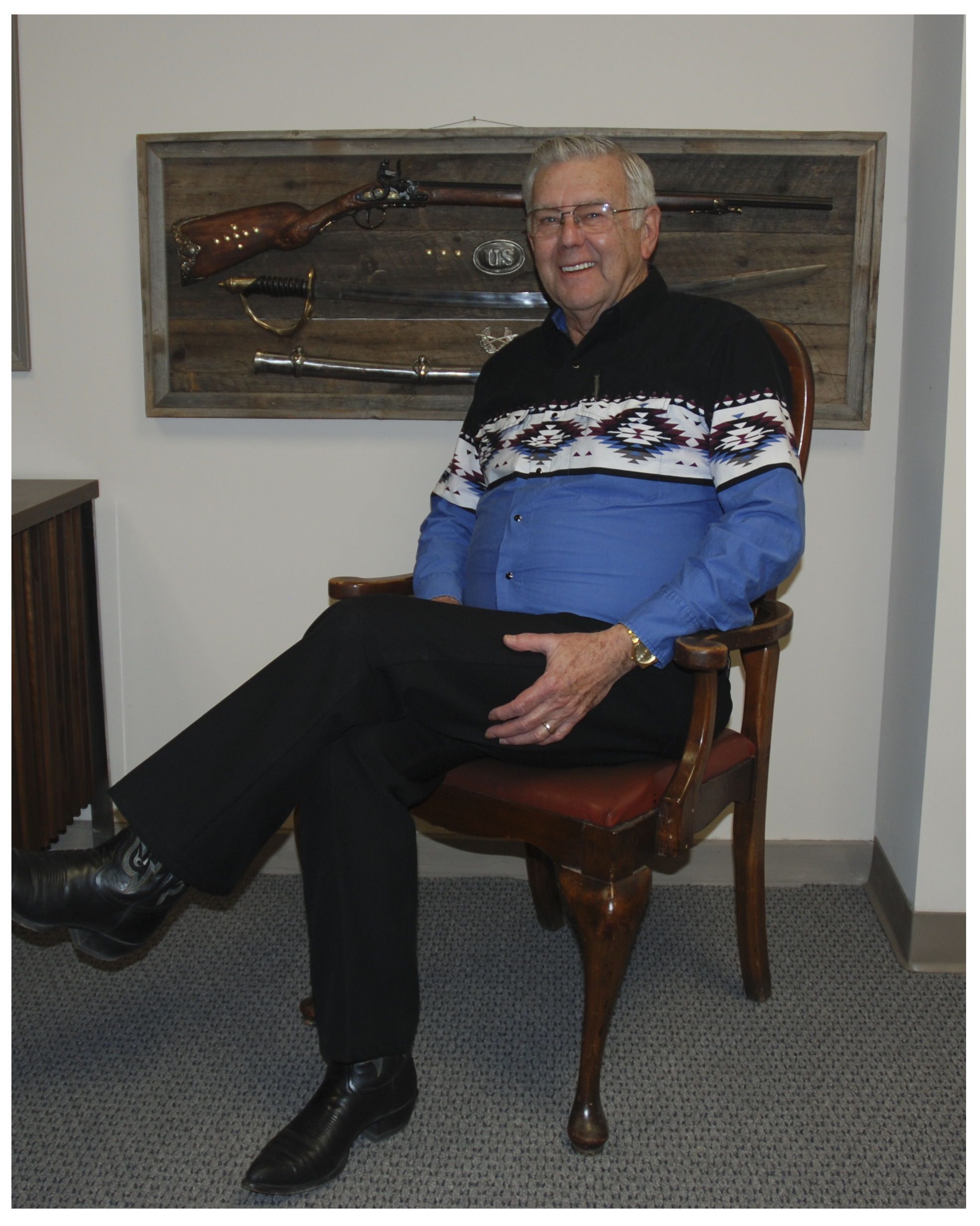 Don Walton sitting in a chair, wearing a patterned sweater, smiling.