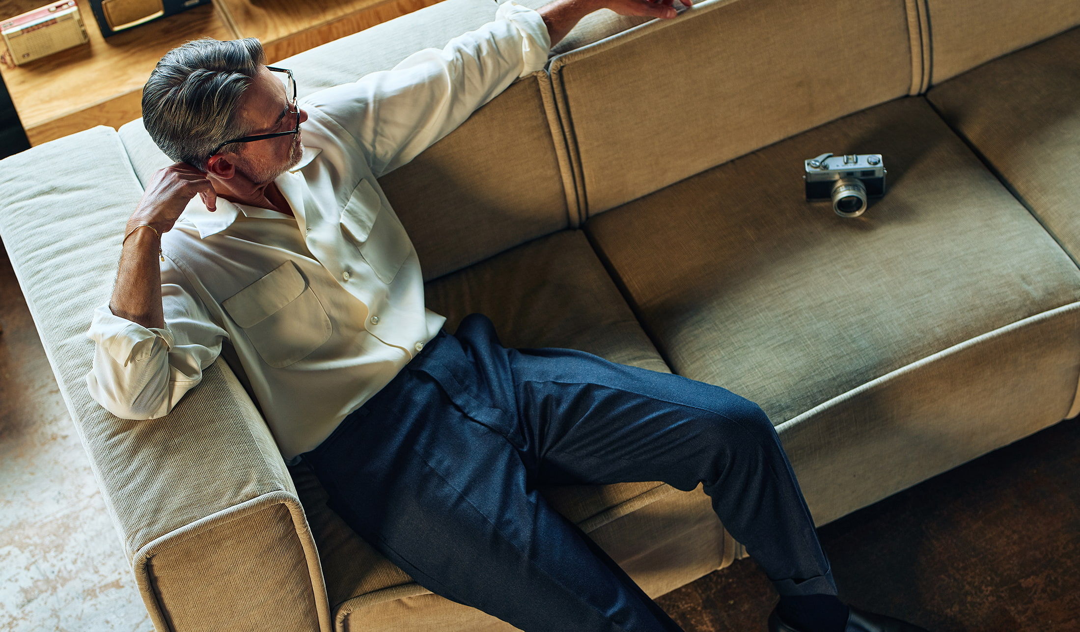 Man sitting on a couch, relaxed, with a small object nearby.
