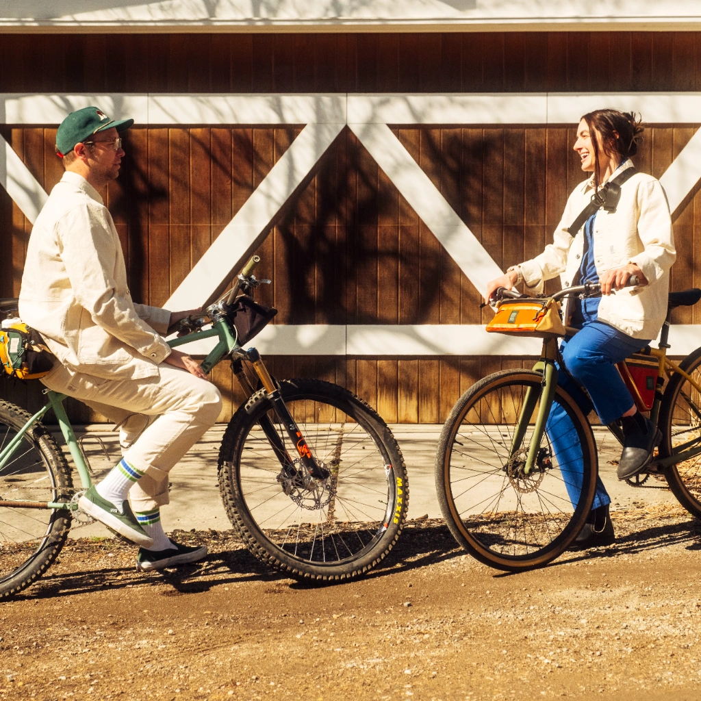 Two people on bicycles chatting near a barn.