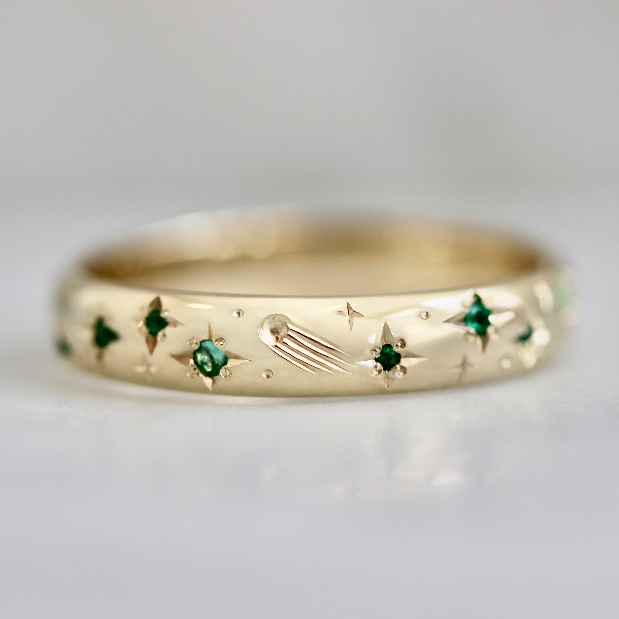 Hand-engraved wedding band with stars, comets, and green sapphires
