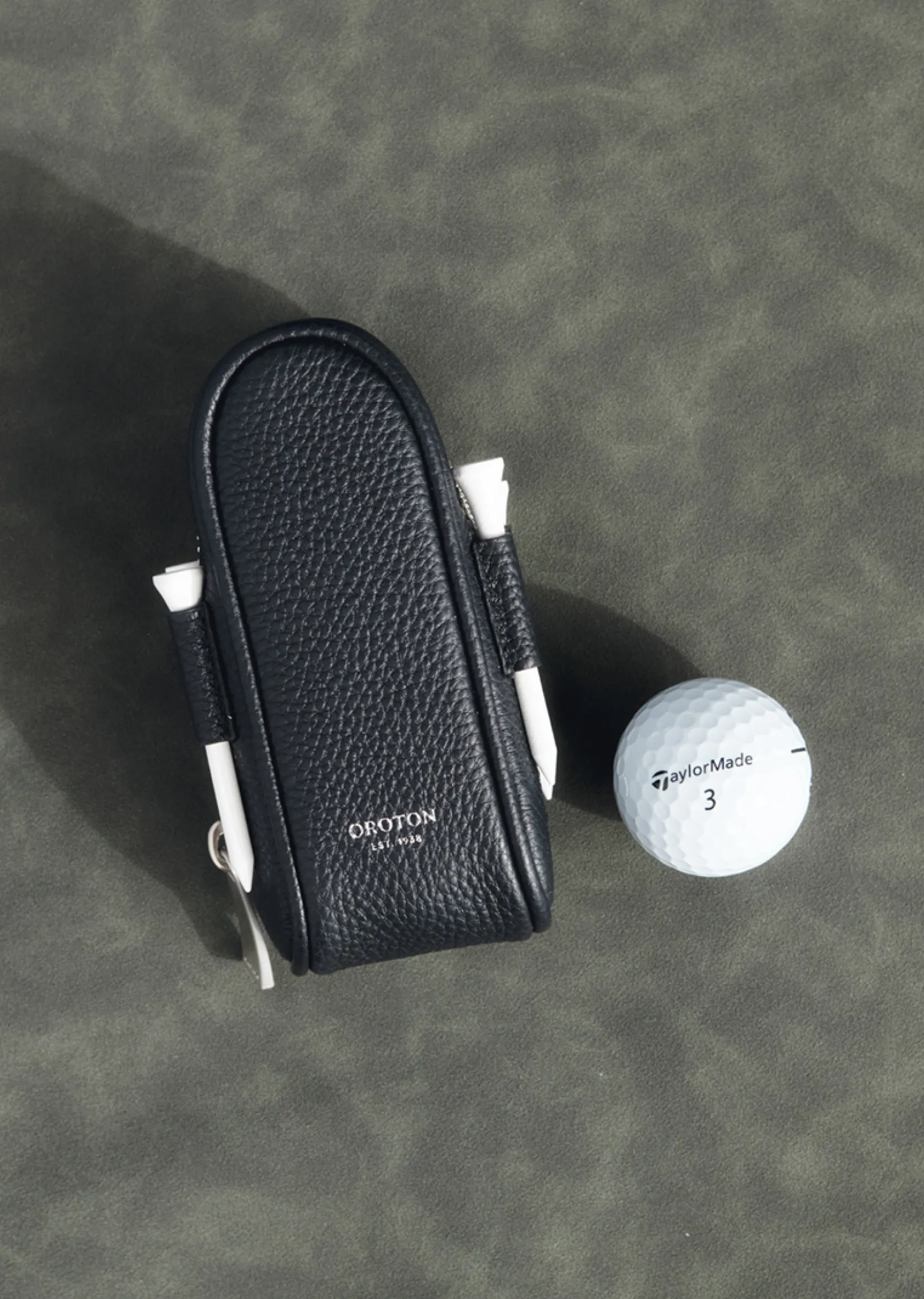A black leather golf tee holder with a golf ball beside it.