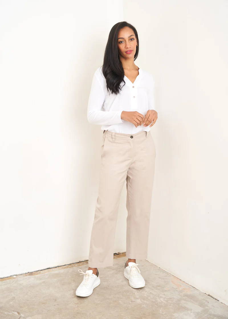 A model wearing a white long sleeved blouse with button neckline, off white trousers and white trainers