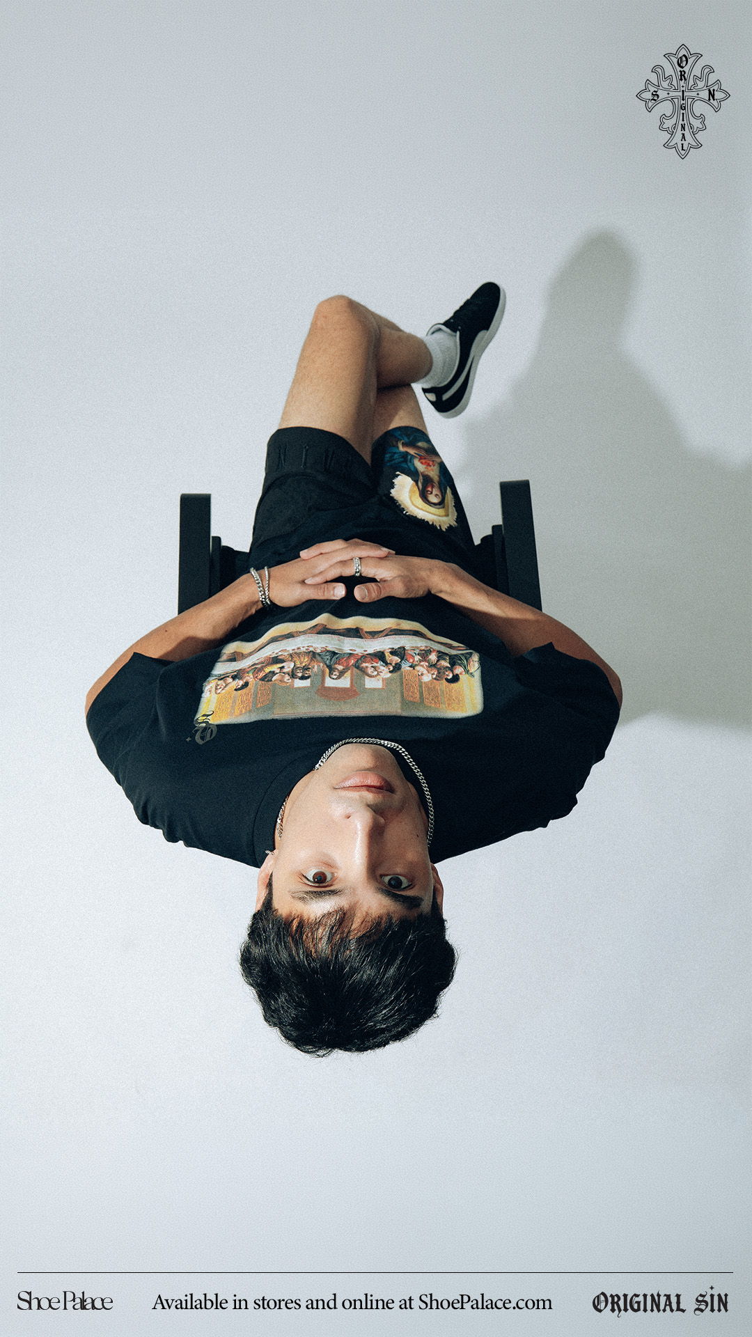 Person sitting on a chair, wearing a graphic t-shirt and shorts.