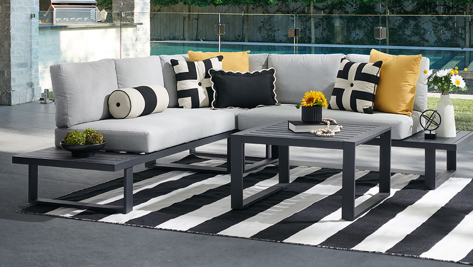Outdoor seating area with a sectional couch, coffee table, and striped rug.