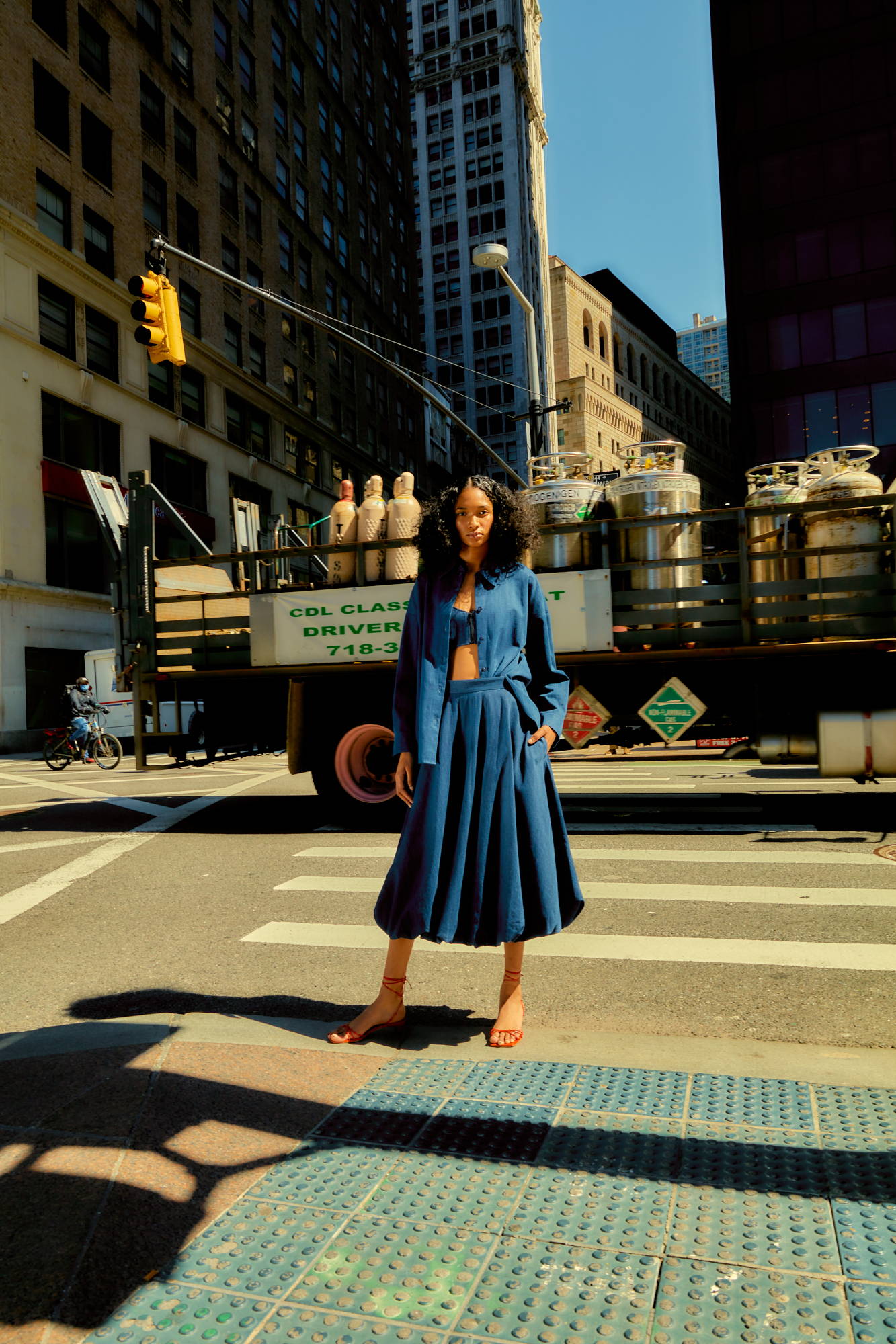 Person in blue outfit standing on a city crosswalk with a truck behind.