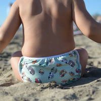 A picture of a baby sitting on the beach with a cloth swim diaper. 