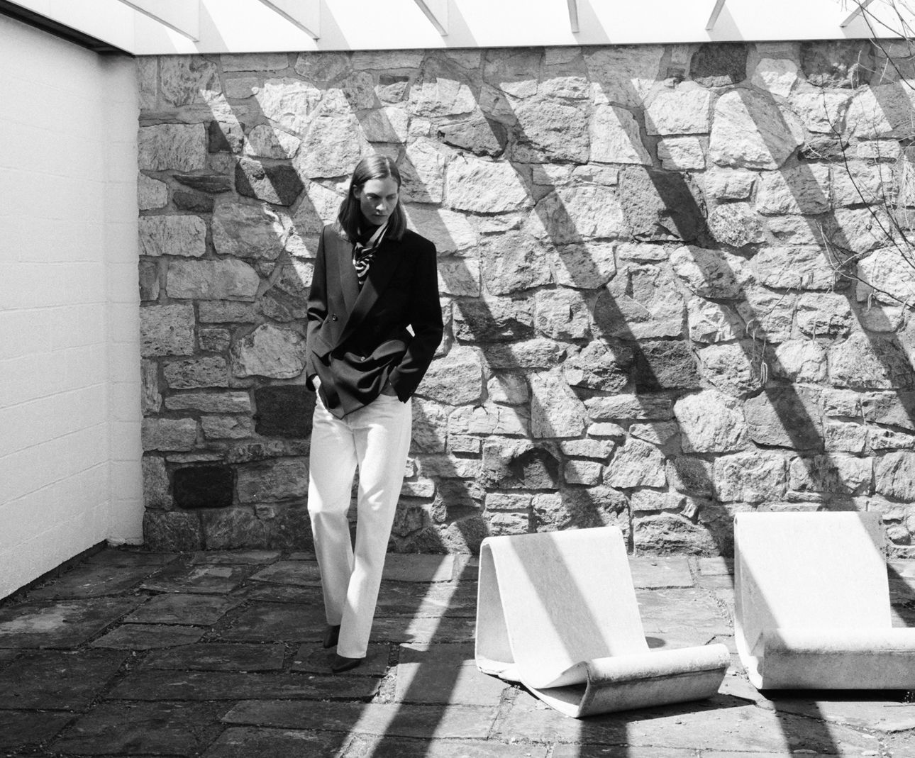 A person standing near a stone wall with sunlight shadows.