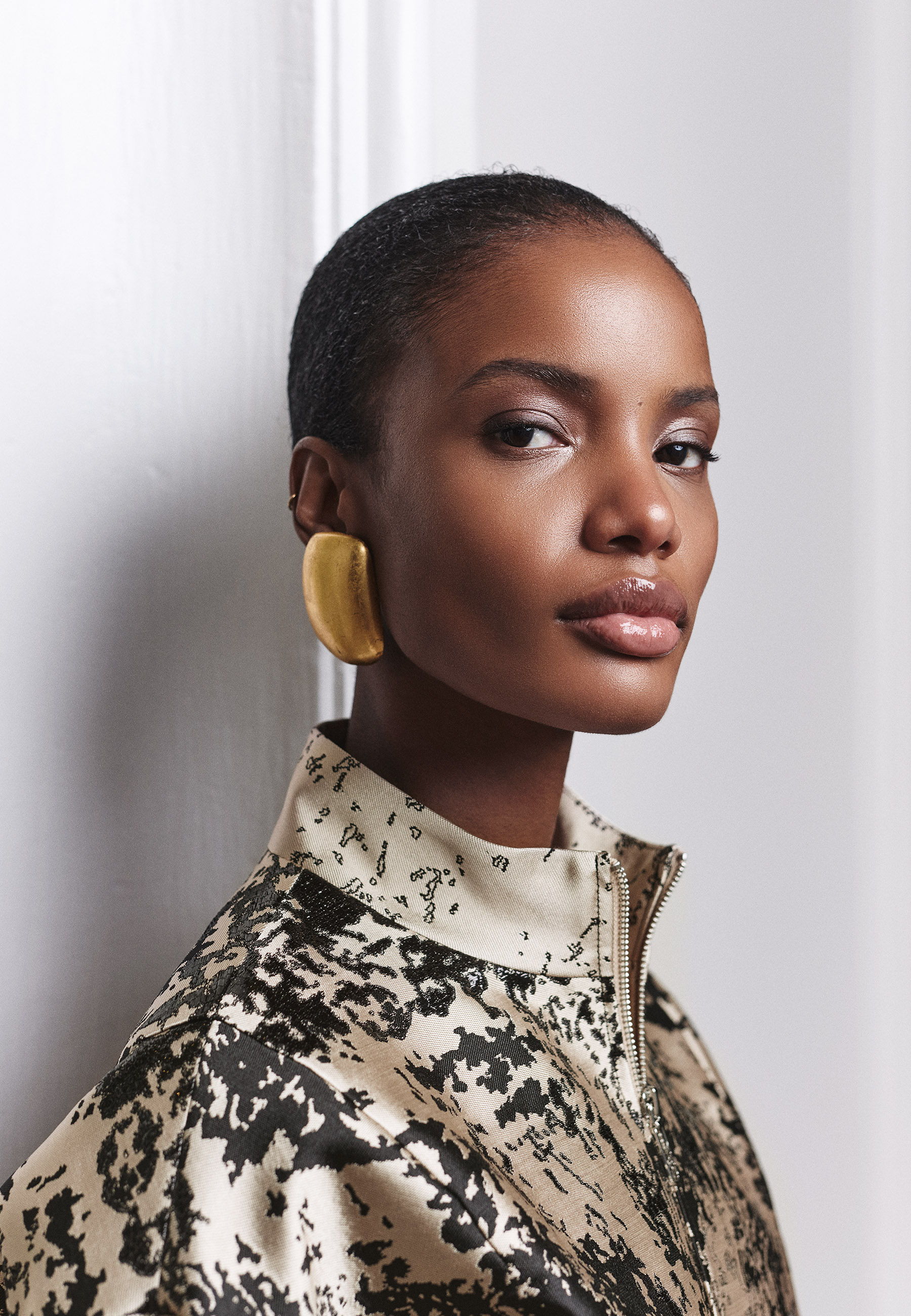A woman in a patterned jacket with bold earrings poses elegantly.