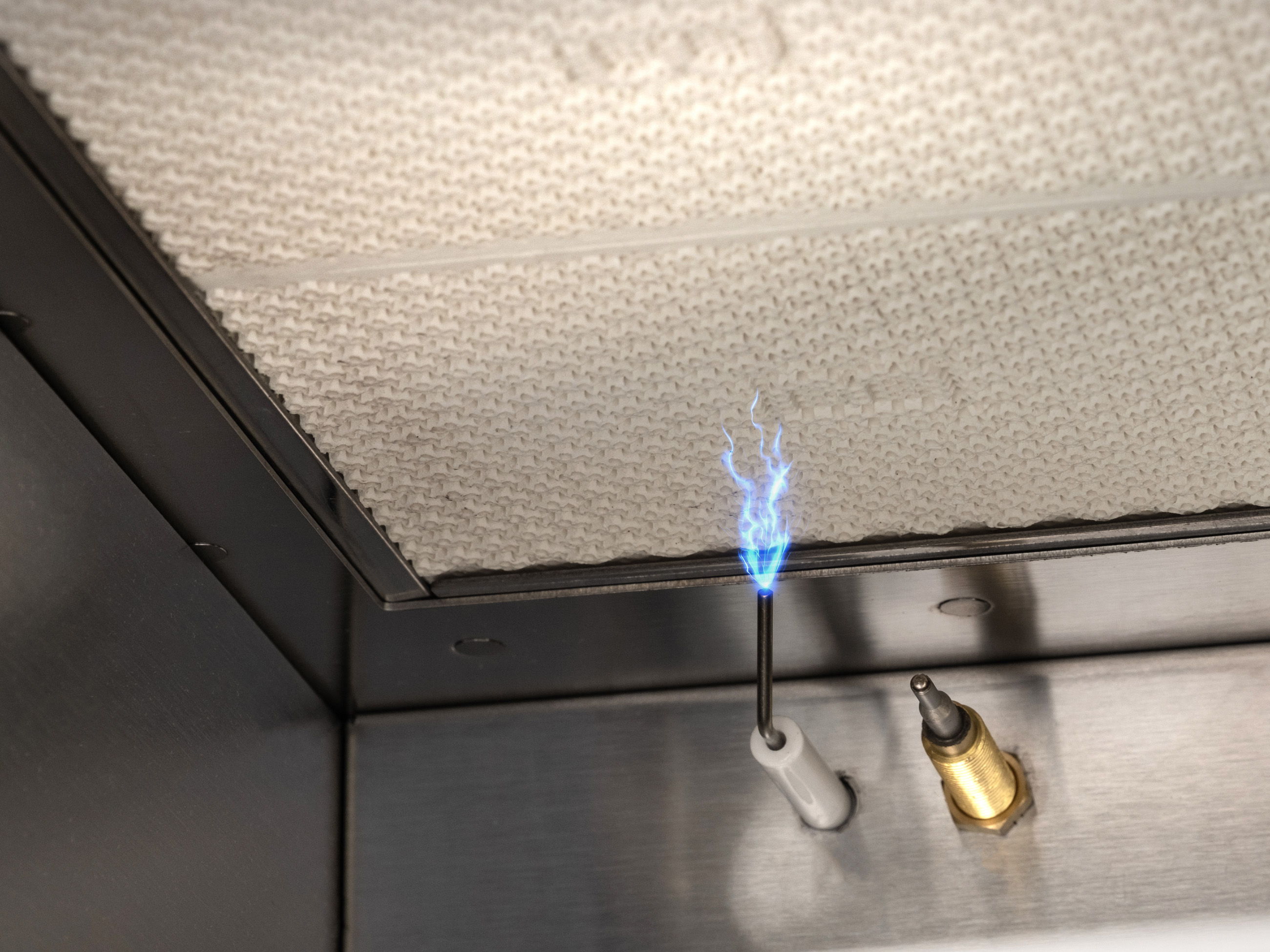 A small blue flame emitting from a metal rod near a textured surface.