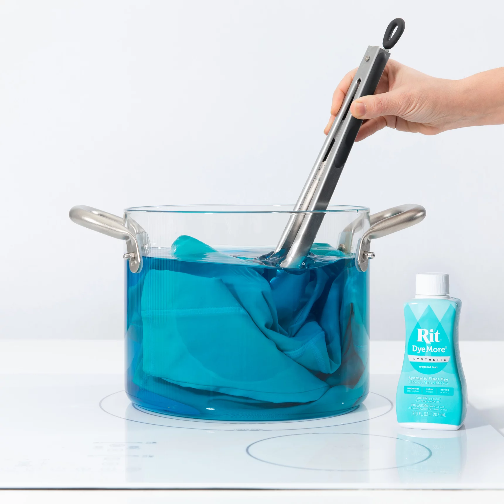 Hand using tongs to dip fabric in blue dye pot.