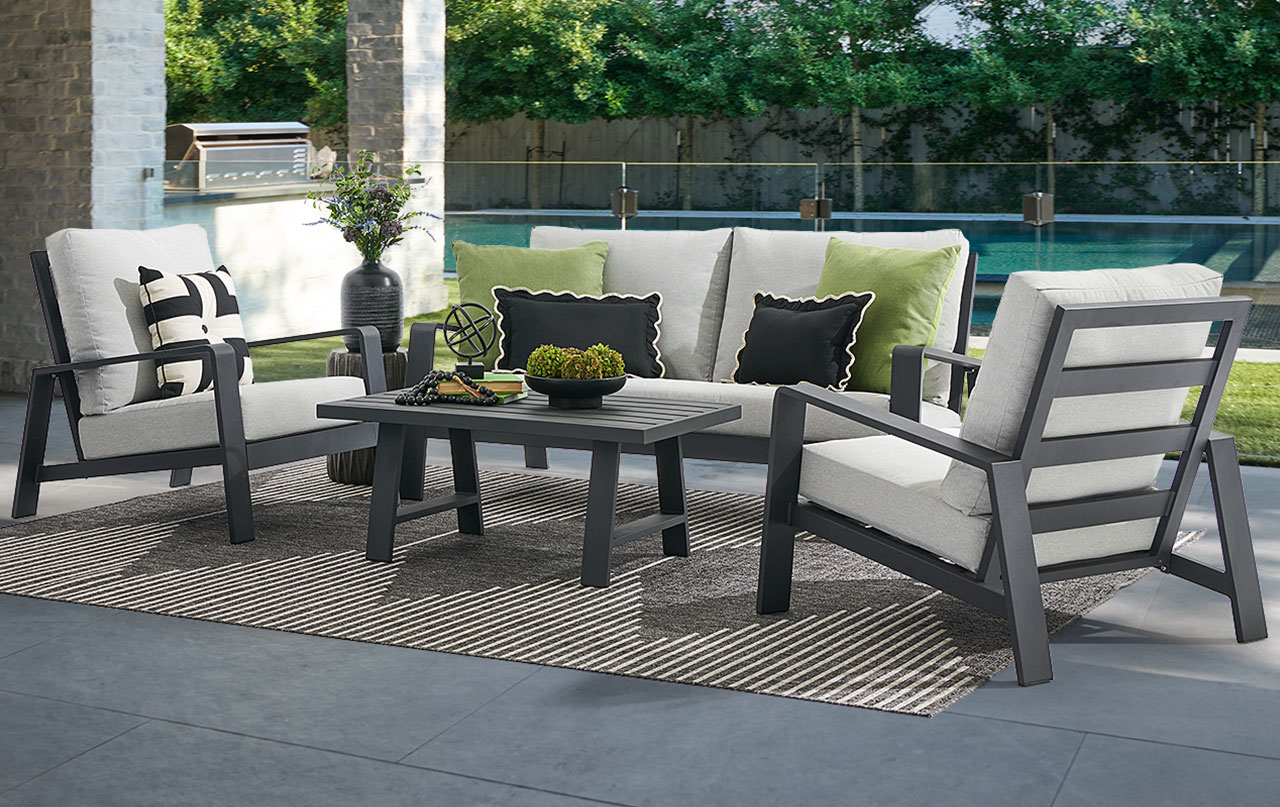 Outdoor seating area with cushions, table, and greenery in the background.