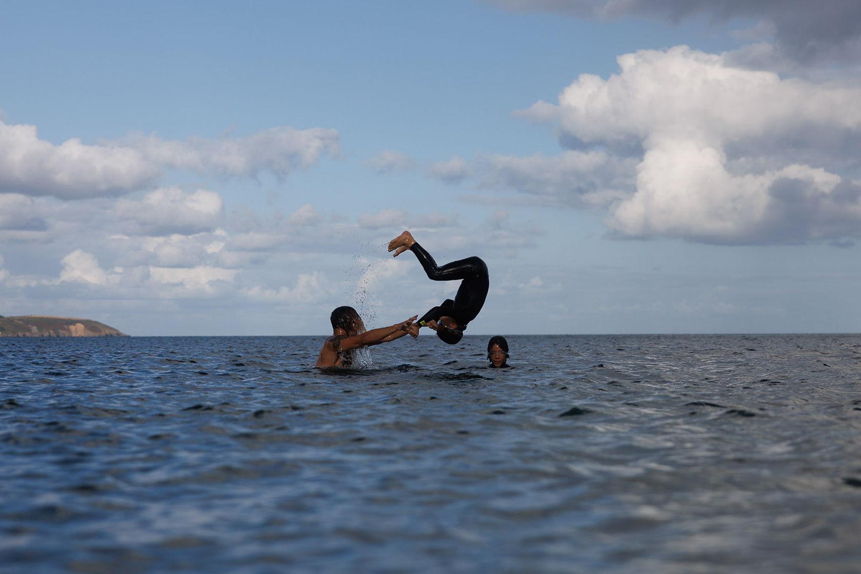 Two people playing in the water, one being tossed into the air.