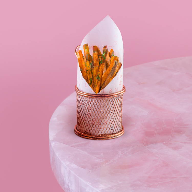 Sweet potato fries on a pink background in a basket