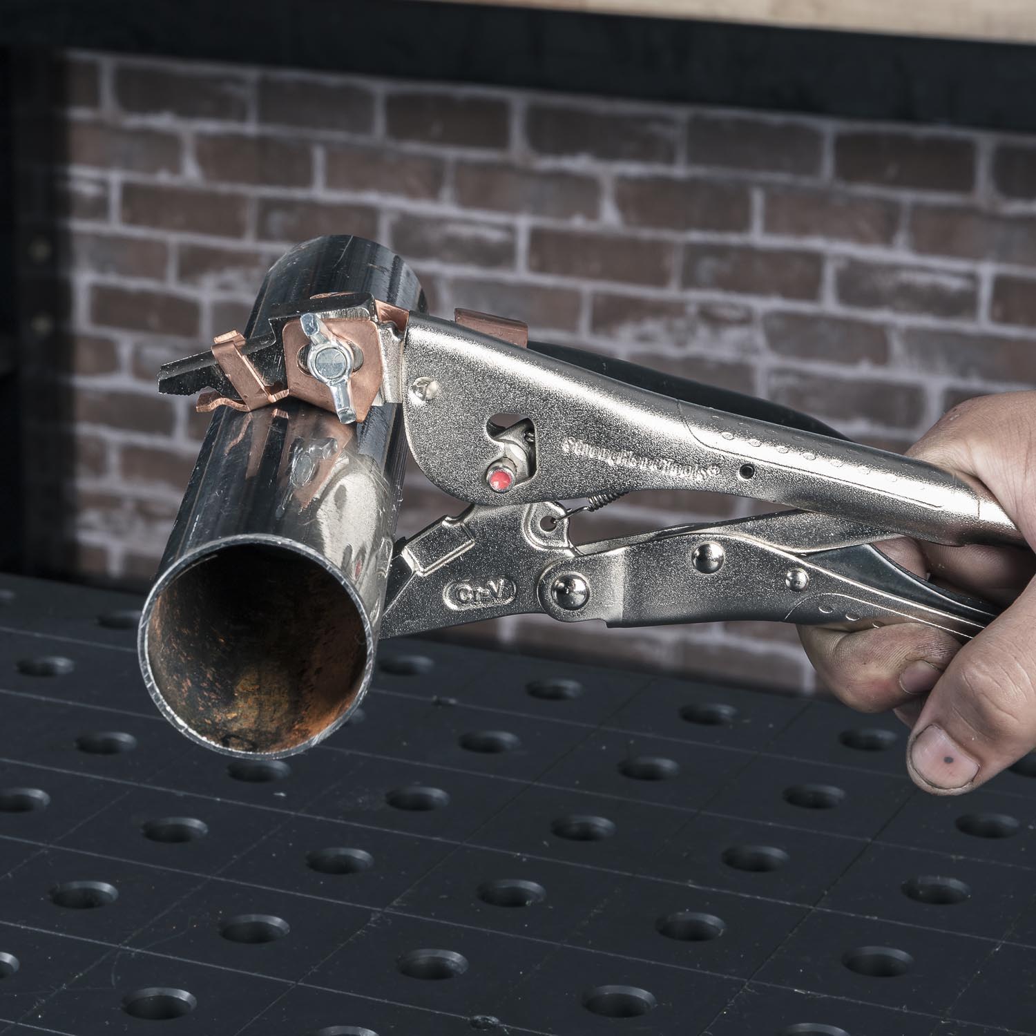 A hand holding a metal clamp on a pipe.