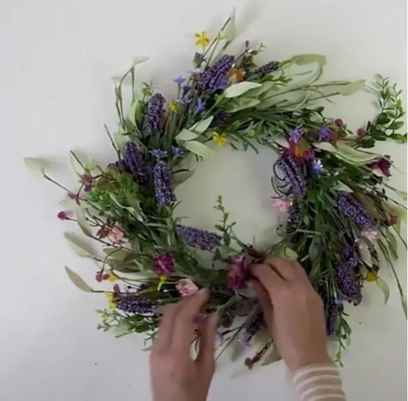 A person fluffing the branches of her spring wreath.