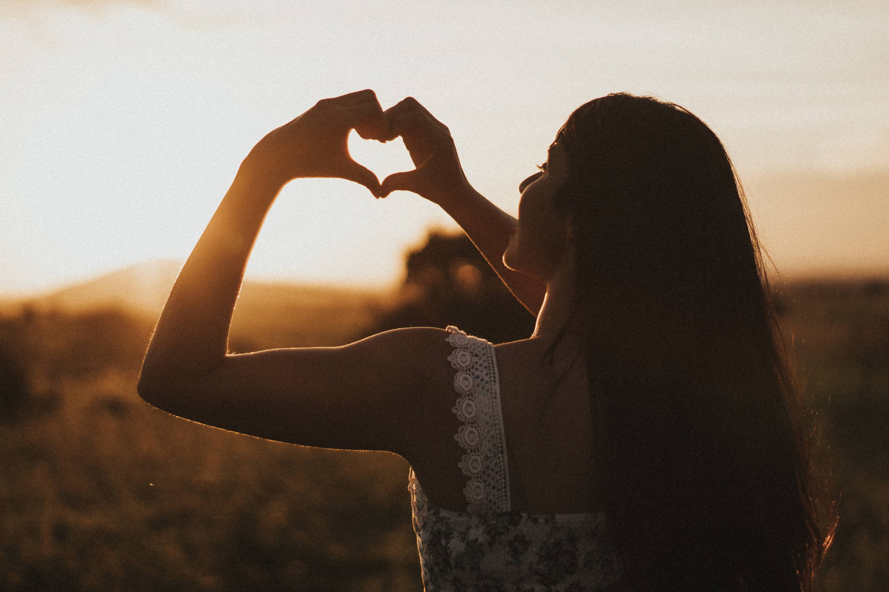woman making heart with hands in sunset
