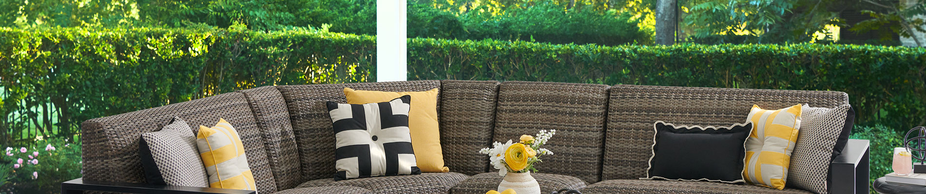Outdoor seating area with decorative cushions and greenery in the background.