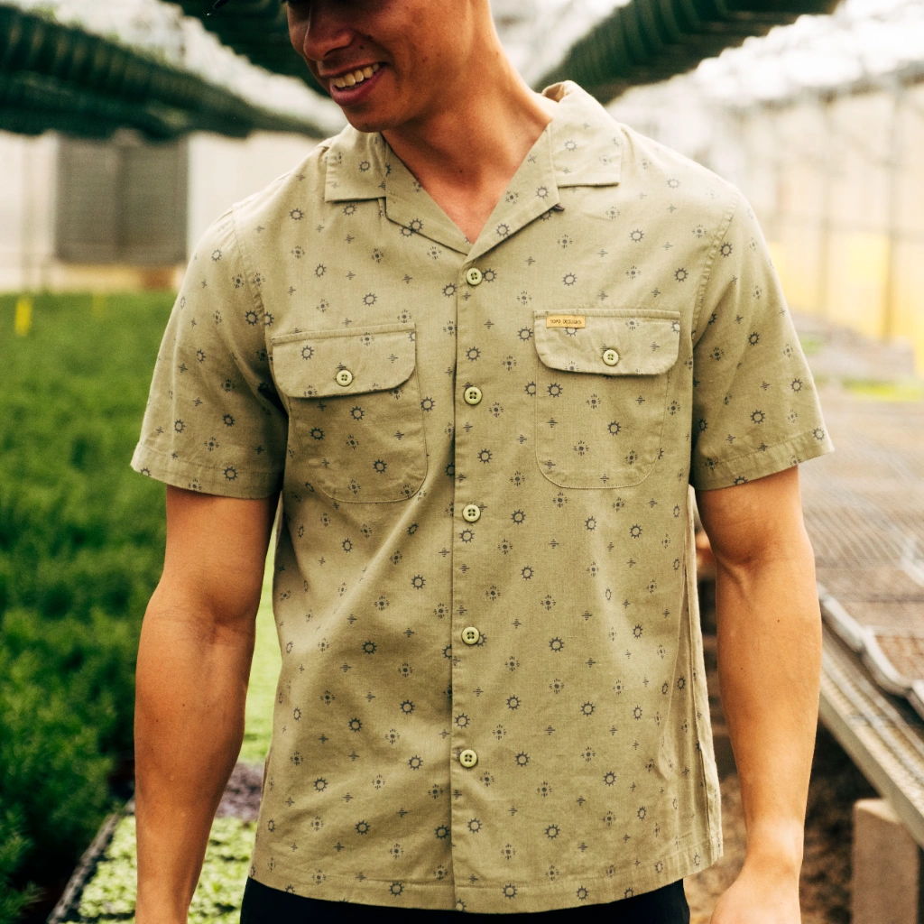 Man in a patterned shirt standing in a greenhouse.