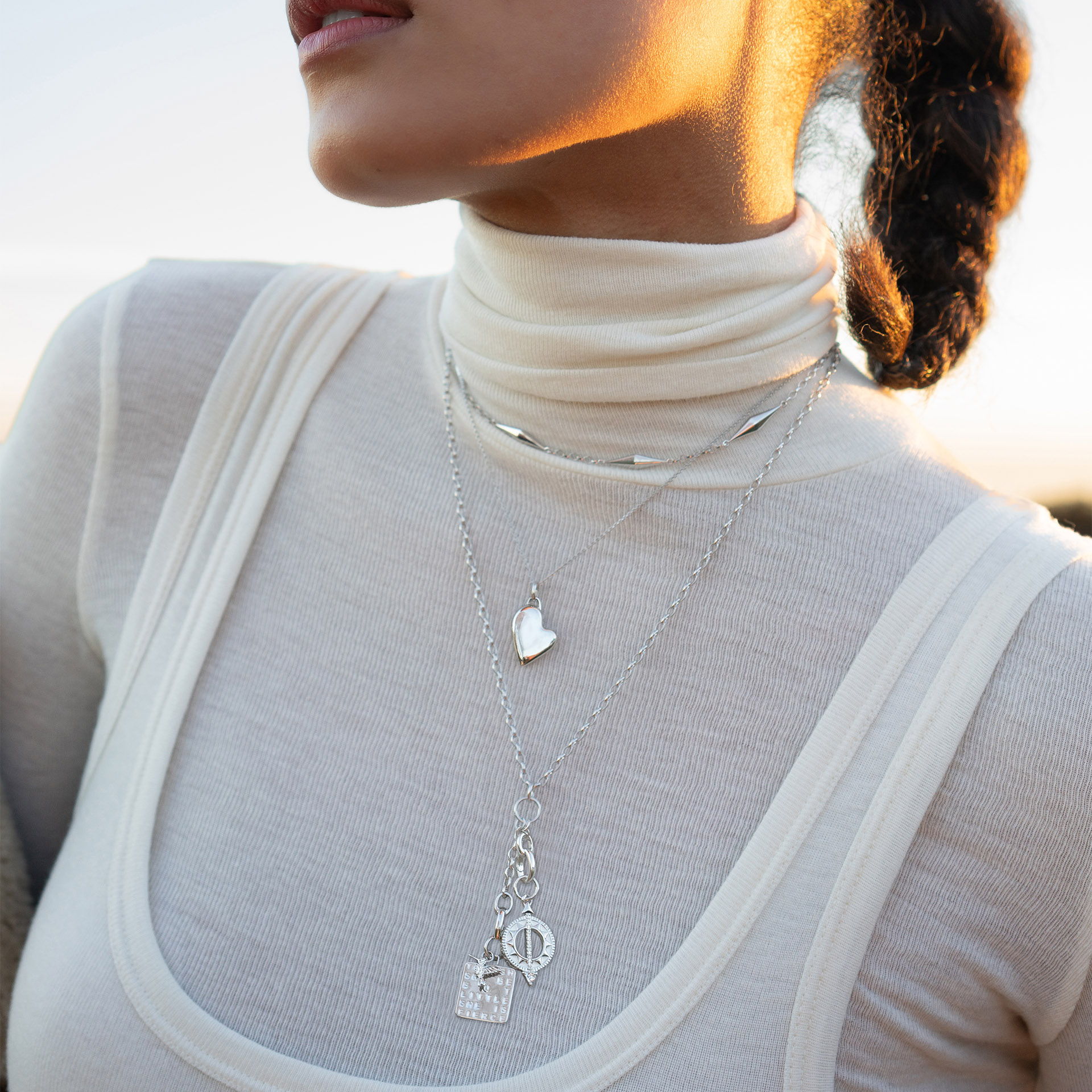 Woman wearing layered silver necklaces and a high-neck top outdoors.