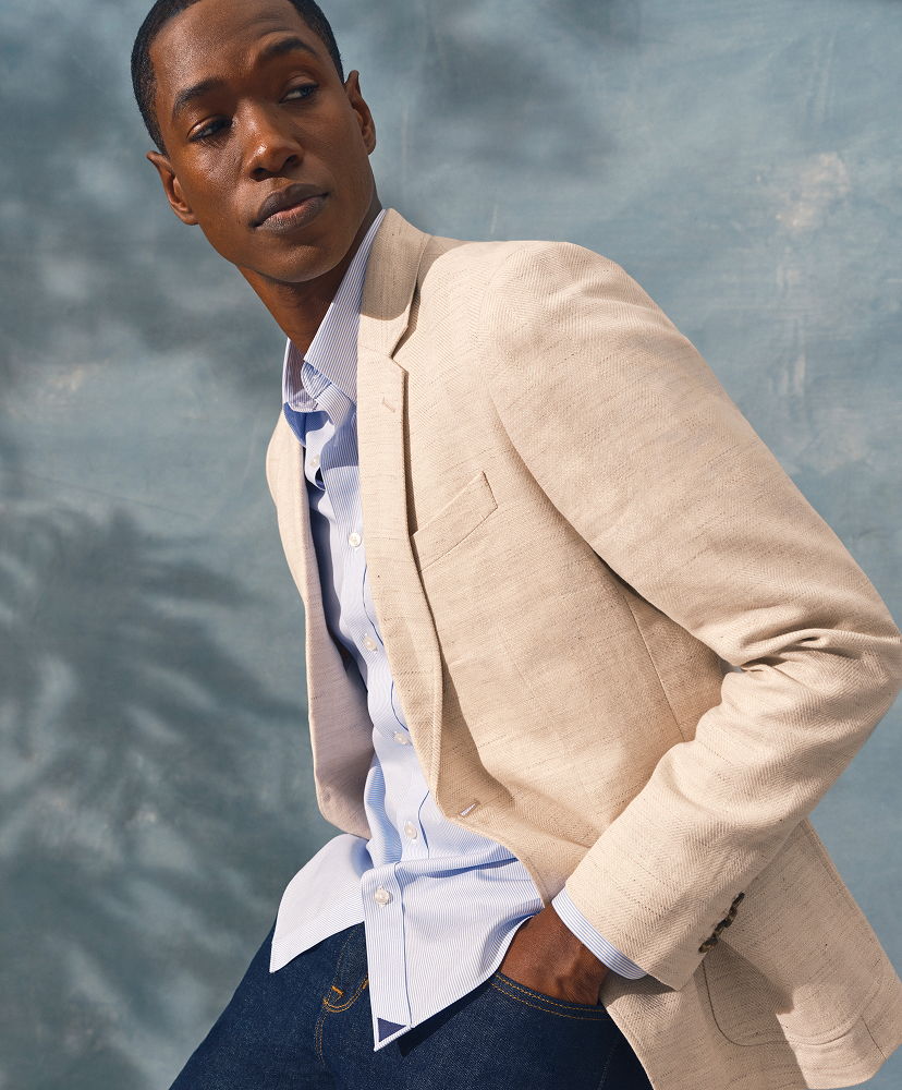 A man in a blazer and shirt poses against a blue background.