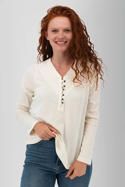 Smiling woman with curly red hair wearing a cream-colored long-sleeve shirt.