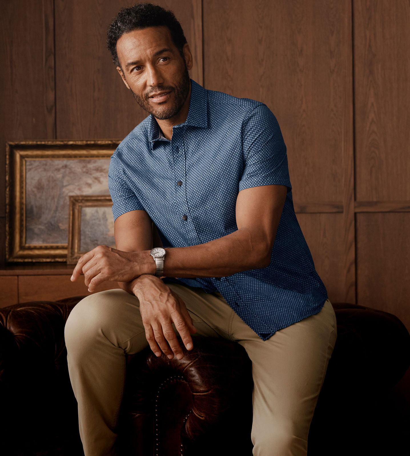 Man in a blue shirt sitting on a couch with a wooden background.