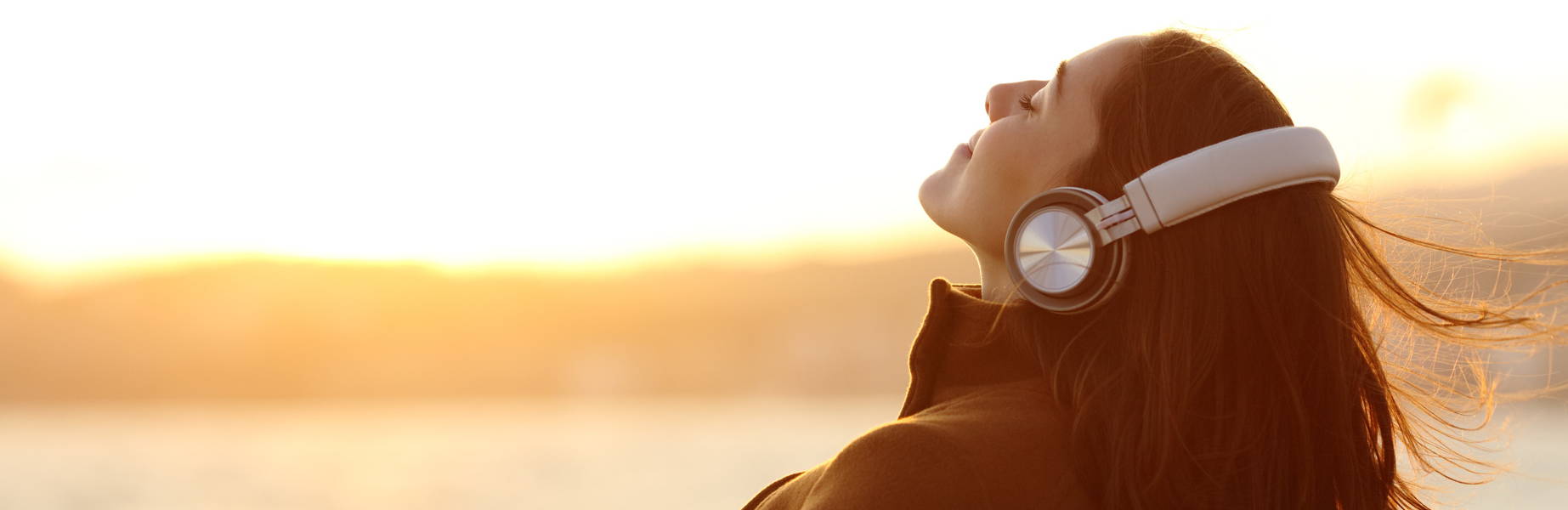 Woman listening to headphones with sunset in  foreground