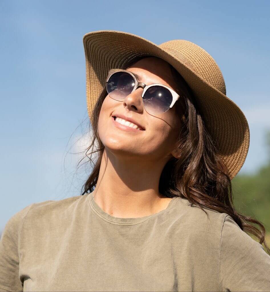 Woman wearing Tom & Cat, Retro-Round Wooden Sunglasses with a straw hat and light grey shirt
