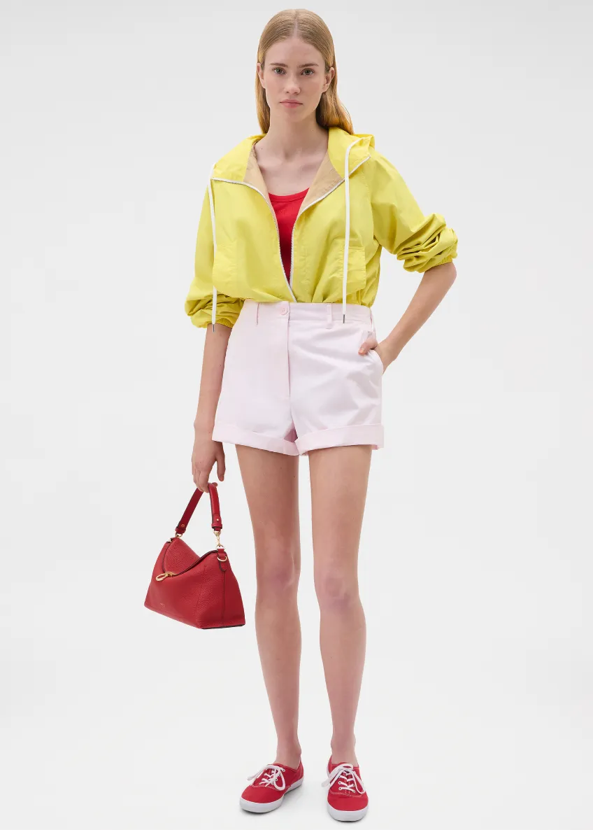 Model in yellow jacket, pink shorts, holding red handbag, wearing red shoes.
