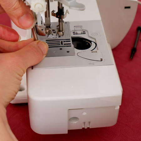 hands with screwdriver to open sewing machine throat plate