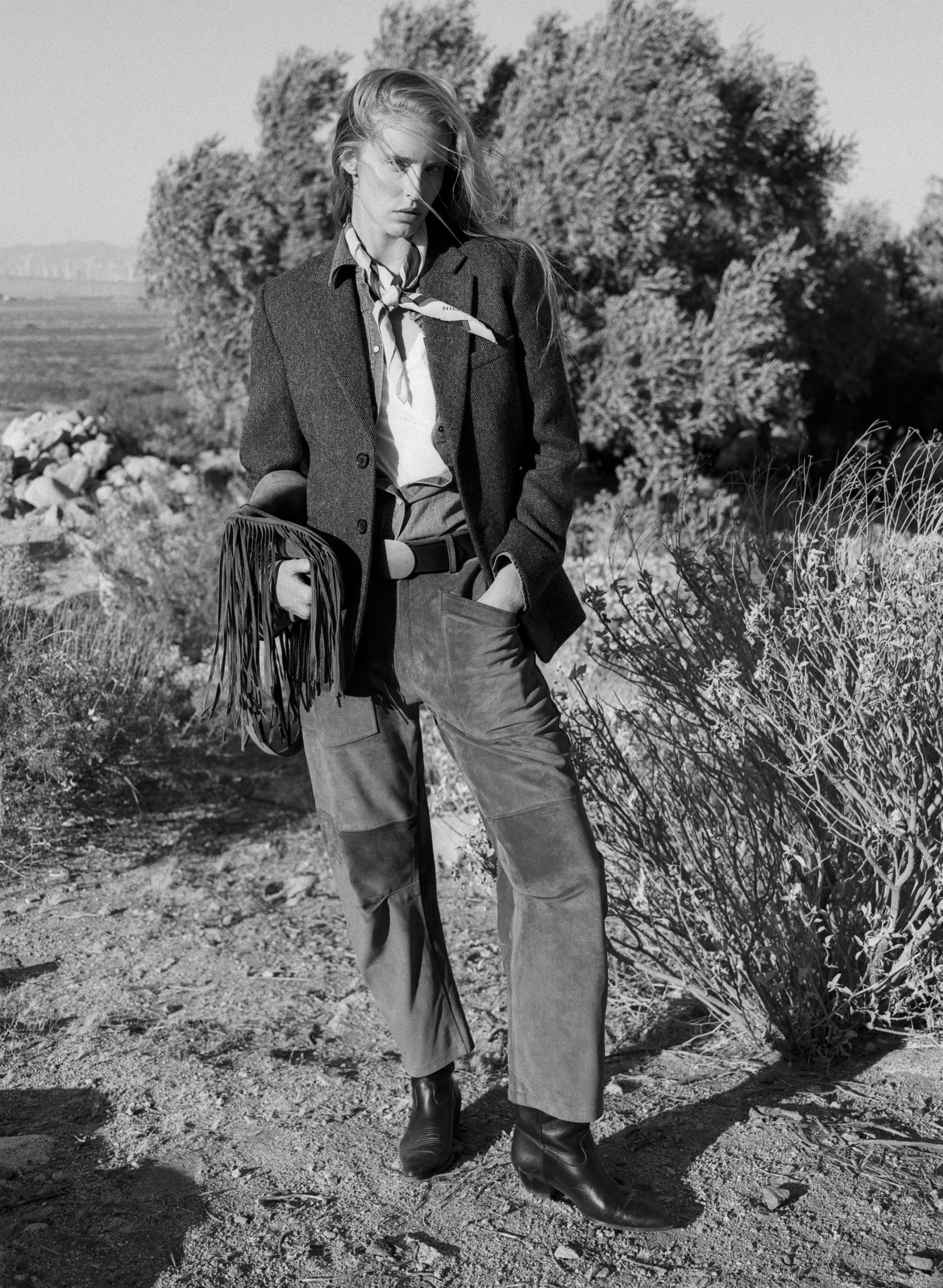 Person in western attire standing outdoors with natural scenery in the background.
