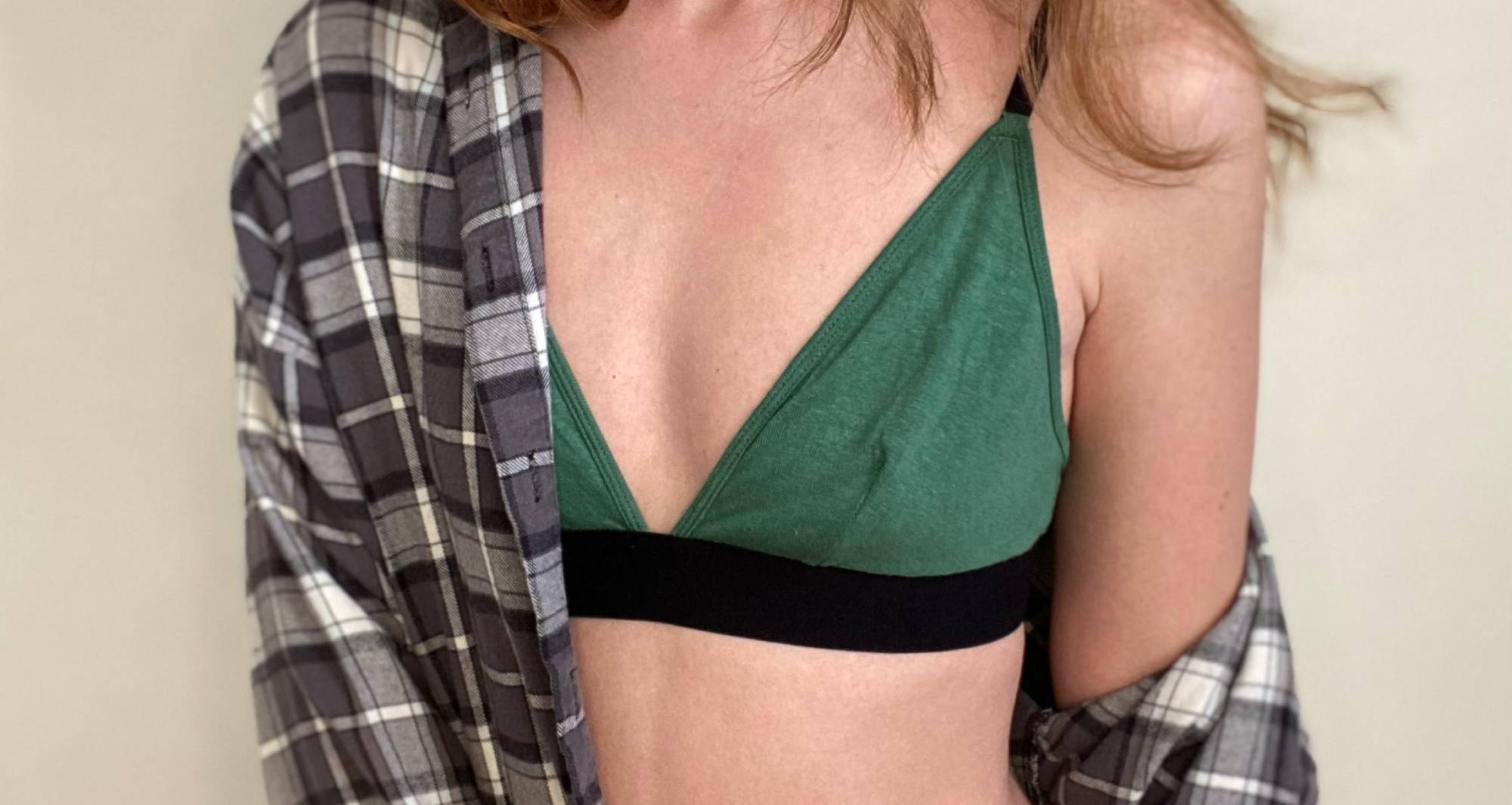 Torso of a woman with red hair wearing a green bralette and an unbuttoned gray plaid shirt