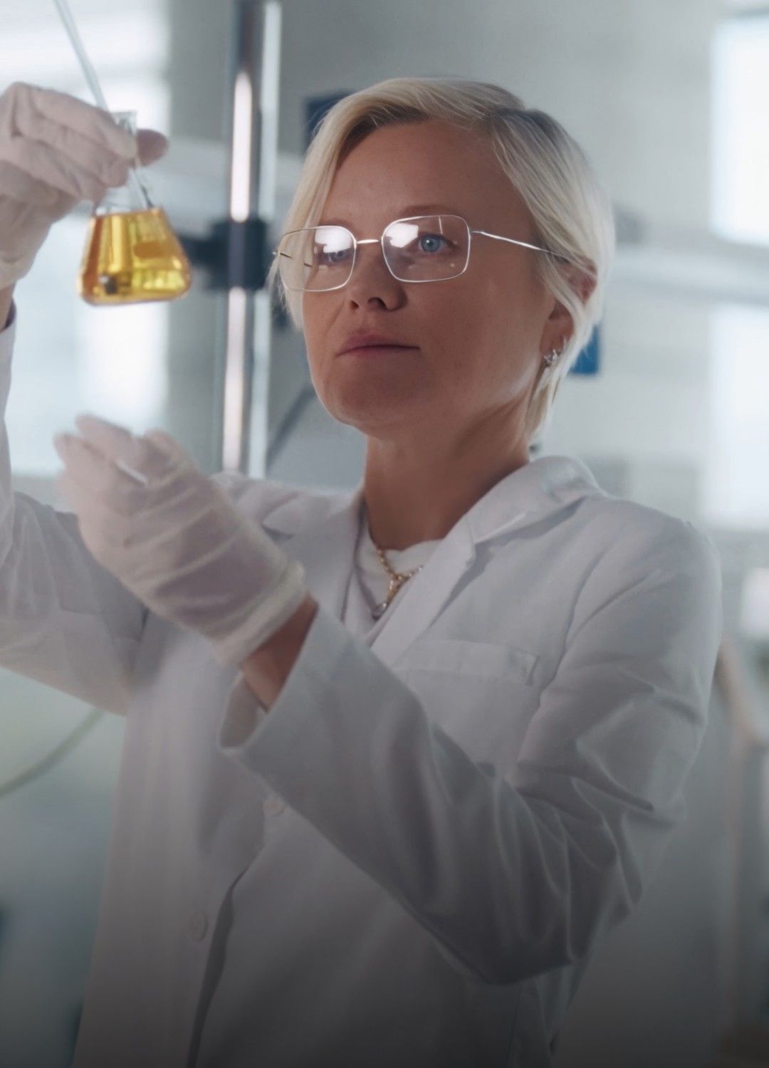 Scientist in lab coat examining a flask of liquid.