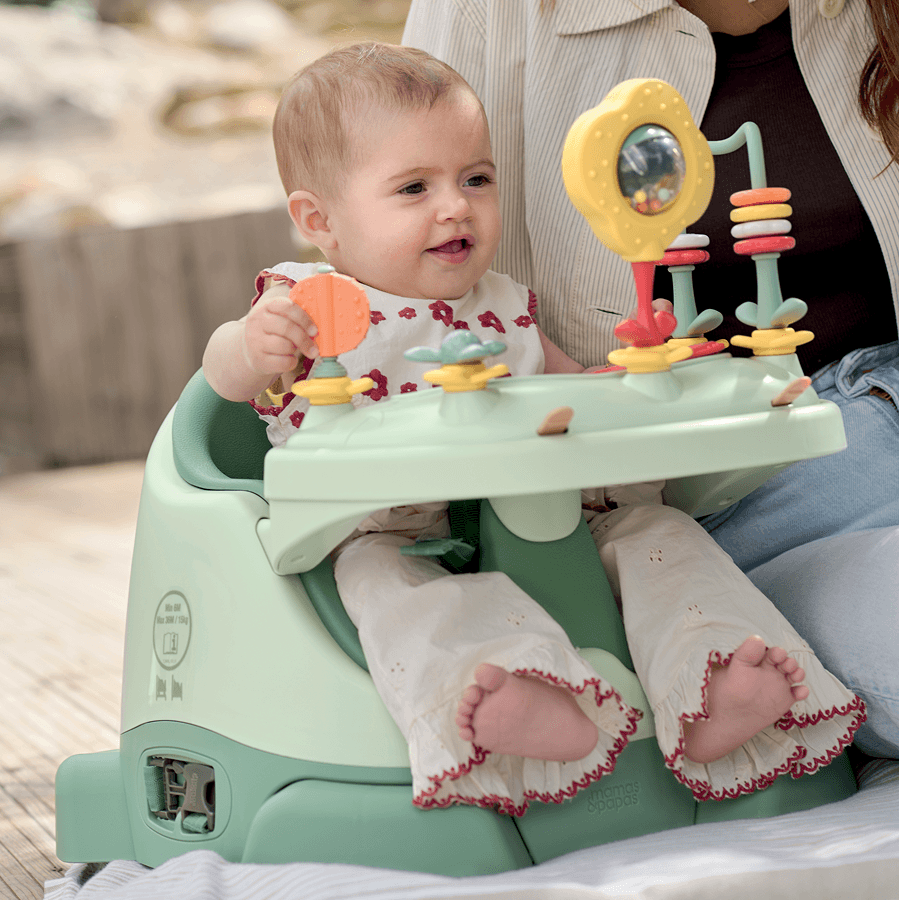 A baby sitting in a high chair playing with colorful toys.