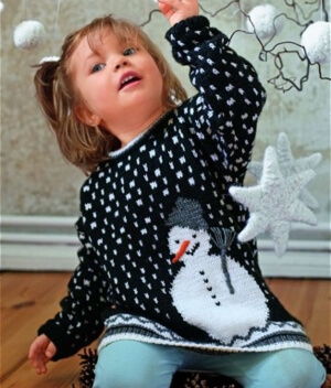 Child in a black sweater with a snowman design, playing with decorations.