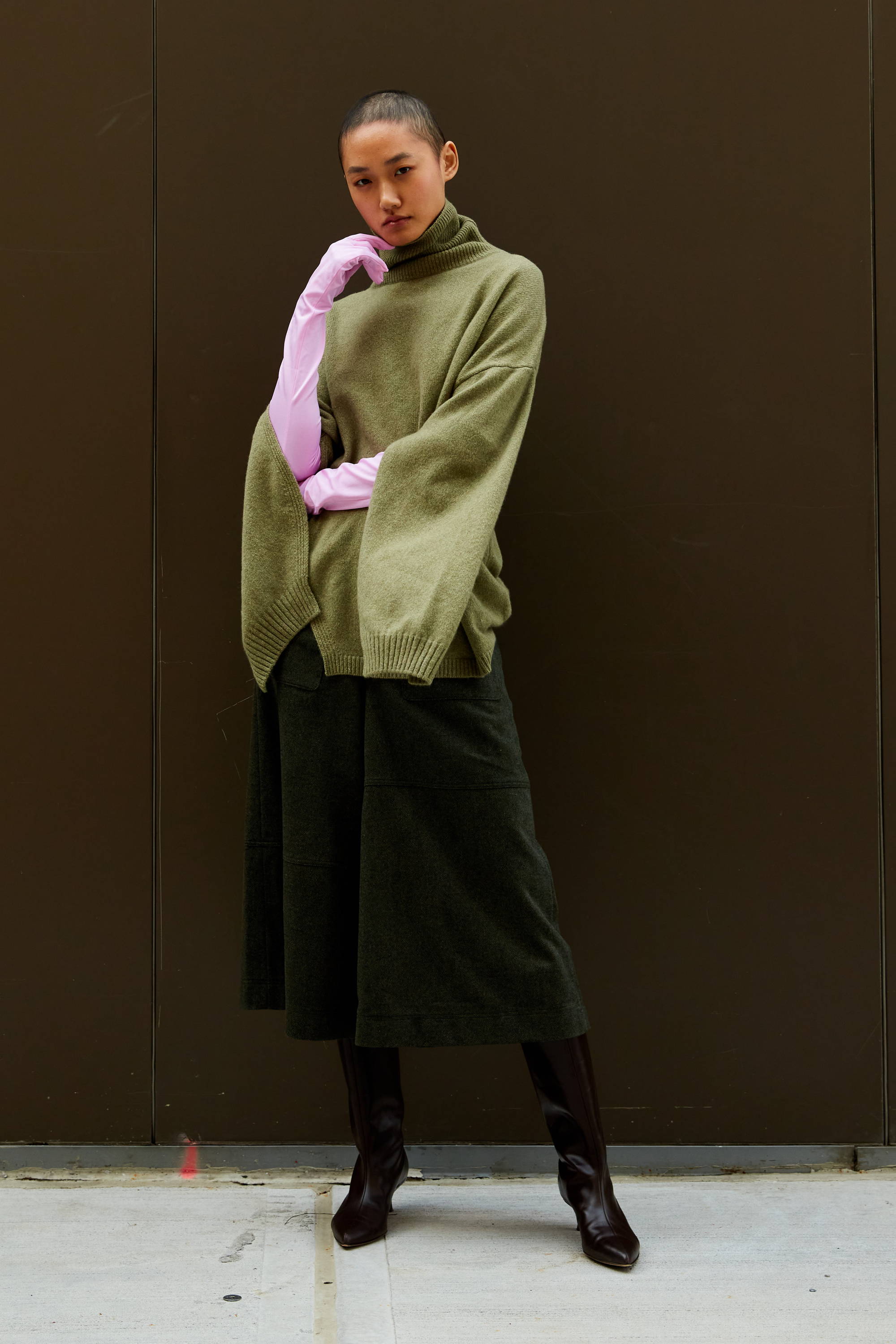Model wearing oversized green sweater and black skirt against a neutral background.